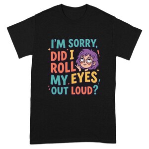 May include: Black t-shirt featuring the phrase "I'M SORRY, DID I ROLL MY EYES, OUT LOUD?" in various colours. The design includes a cartoon of a person with purple hair, glasses, and a bored expression.