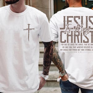May include: White t-shirts with religious text and imagery. One shirt features a cross graphic on the front. The other shirt displays the text "JESUS Is King CHRIST" on the back, along with a Bible verse from John 3:16.