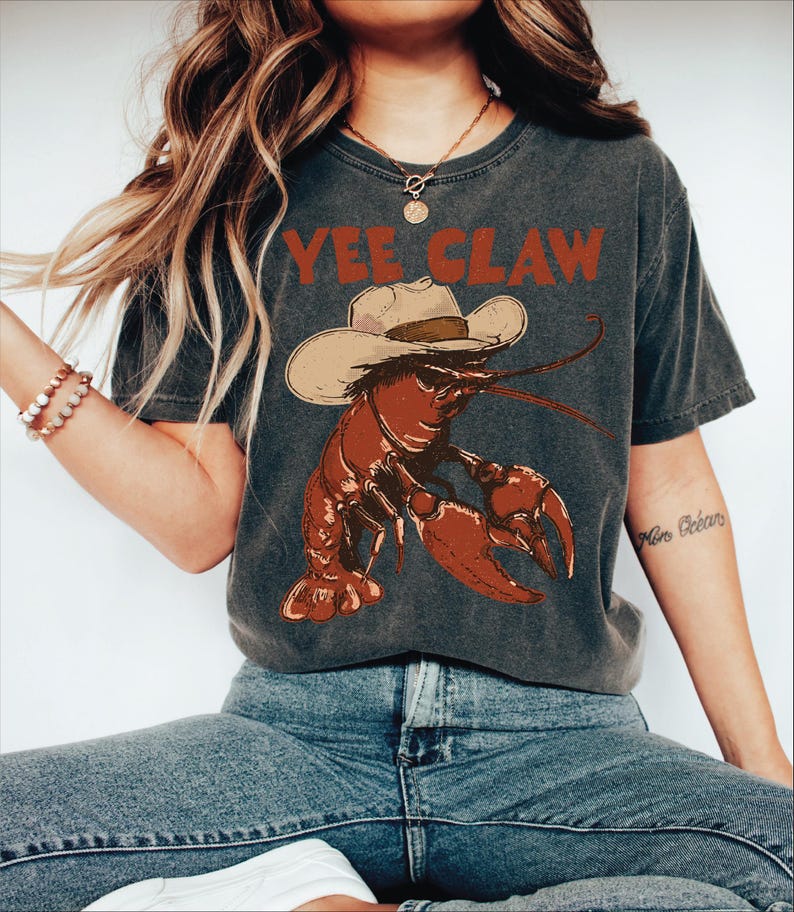 A woman wearing a gray t-shirt with a lobster graphic and the text "YEE CLAW" printed on it.