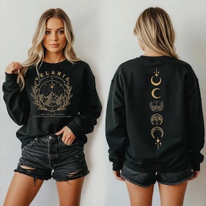 May include: Black sweatshirt with gold text and graphics. The front features the text "VELARIS CITY OF STARLIGHT" within a circular design with mountains. The back has a vertical design of crescent moons and stars.