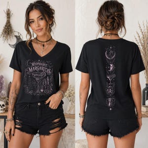 May include: A black V-neck t-shirt featuring a white graphic print on the front that reads Midnight Margaritas with a cocktail glass and celestial elements. The back of the shirt displays a vertical column of white illustrations including moons.