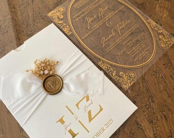 Pode incluir: Convite de casamento elegante com um cartão branco, monograma dourado e a data "27 OUTUBRO 2025". Um selo de cera dourada e uma fita branca adornam a frente. Um cartão transparente com detalhes florais dourados e texto é visível.