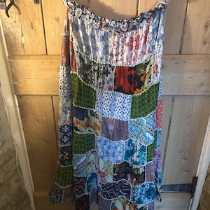May include: A patchwork skirt with a variety of colorful fabric patterns, including floral, geometric, and abstract designs. The skirt is hanging on a wooden hanger, showcasing its full length and the intricate details of the fabric.