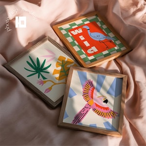 May include: Three wooden frames containing art prints. One print features a blue heron on an orange background with the text "WILD" over a green and white checkerboard. Another shows green and yellow tropical leaves. The third displays a pink parrot.