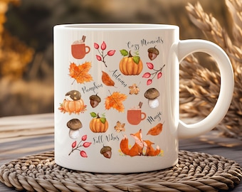 May include: White ceramic mug featuring autumn-themed illustrations. The design includes pumpkins, fall leaves, acorns, mushrooms, and a fox. Text elements include "Cozy Moments," "Autumn," "Pumpkin," "Magic," and "Fall Vibes."