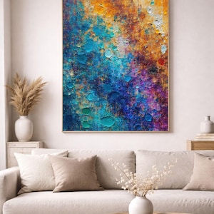 May include: Abstract art print with a textured, colourful design. The artwork features a blend of blues, oranges, and purples, with a wooden frame. The painting is displayed above a beige sofa with decorative cushions, enhancing the room's decor.