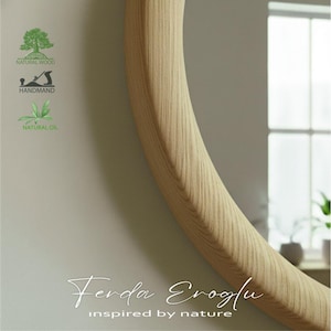 Close-up view of a handmade round mirror with a solid oak wooden frame, highlighting its natural texture and smooth, minimalist curves.