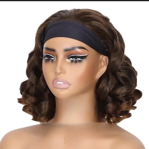 Peut inclure: Tête de mannequin avec une perruque brune bouclée et un bandeau noir. Le mannequin porte un maquillage des yeux saisissant avec un eye-liner blanc et de longs cils. Les lèvres sont d'un rose pâle. La perruque a un aspect naturel.
