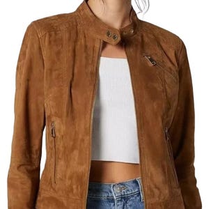 May include: A brown suede jacket with a stand-up collar and a front zip. The jacket features two zipped pockets and a tailored fit. The jacket is worn with a white top and blue jeans.
