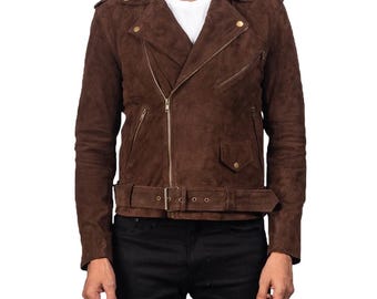May include: A brown suede jacket with a classic biker style. The jacket features a notched collar, an asymmetrical zipper closure, and a belt at the waist. The jacket has a soft, textured appearance and is worn over a white t-shirt and black jeans.