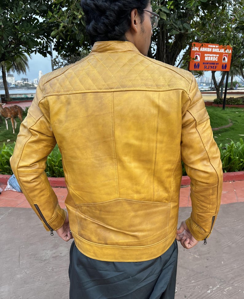 K&ouml;nnte beinhalten: Senfgelbe Lederjacke mit Steppung an den Schultern und Rei&szlig;verschl&uuml;ssen an den &Auml;rmeln. Die Jacke hat einen klassischen Biker-Stil mit Stehkragen und taillierter Passform. Die R&uuml;ckansicht zeigt die Details der Jacke, einschlie&szlig;lich der N&auml;hte.