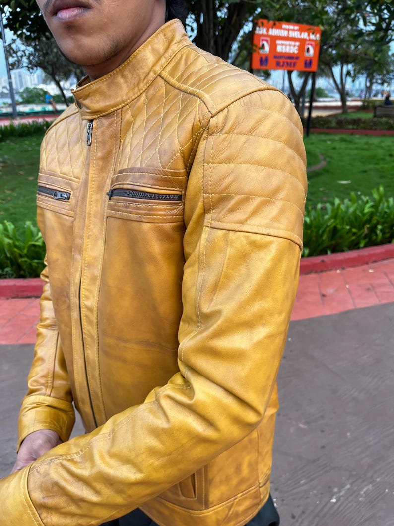 K&ouml;nnte beinhalten: Senfgelbe Lederjacke mit einem gesteppten Schulterdesign und zwei Brusttaschen mit Rei&szlig;verschluss. Die Jacke hat einen Stehkragen und einen Frontrei&szlig;verschluss. Die &Auml;rmel sind lang und tailliert, und das Leder hat ein leichtes Used-Look-Aussehen.