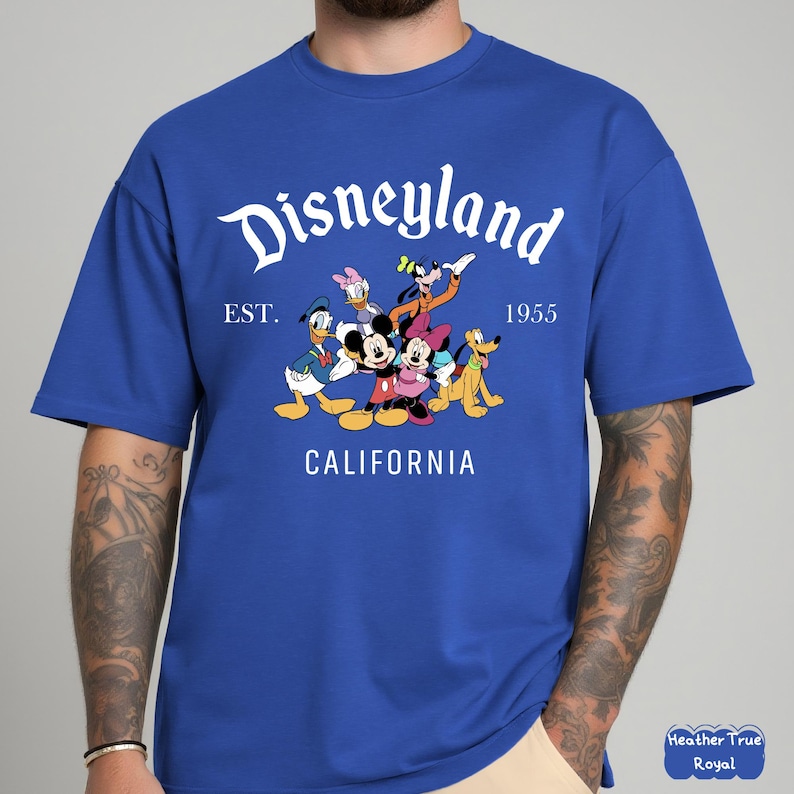May include: Royal blue t-shirt featuring the Disneyland logo with Mickey Mouse, Minnie Mouse, Donald Duck, Goofy, Pluto, and Daisy Duck. The shirt includes the text "EST. 1955 CALIFORNIA".