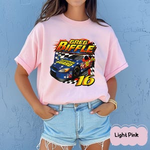 May include: Pale pink t-shirt with a racing car graphic, the text "Greg Biffle", and the number "16". The car design includes "National Guard" and a chequered flag pattern.
