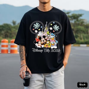 May include: Black t-shirt featuring a colorful graphic of Disney characters, including Mickey and Minnie Mouse, Goofy, and Donald Duck, with a castle and the text "Disney Trip 2020". The shirt has short sleeves.