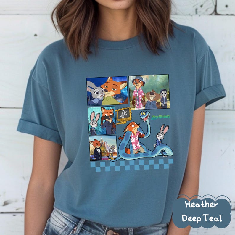 May include: Heather Deep Teal t-shirt featuring a colorful graphic of characters from the animated movie Zootopia. The design includes multiple panels with images of a fox, a bunny, and other characters. The word "Zootopia" is also visible.