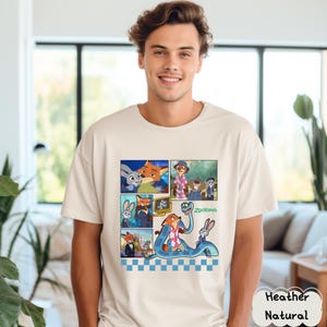 May include: A heather natural t-shirt featuring a colorful comic strip design with characters from the animated movie "Zootopia." The design includes images of a fox, a rabbit, and other characters. The word "Zootopia" is also visible.