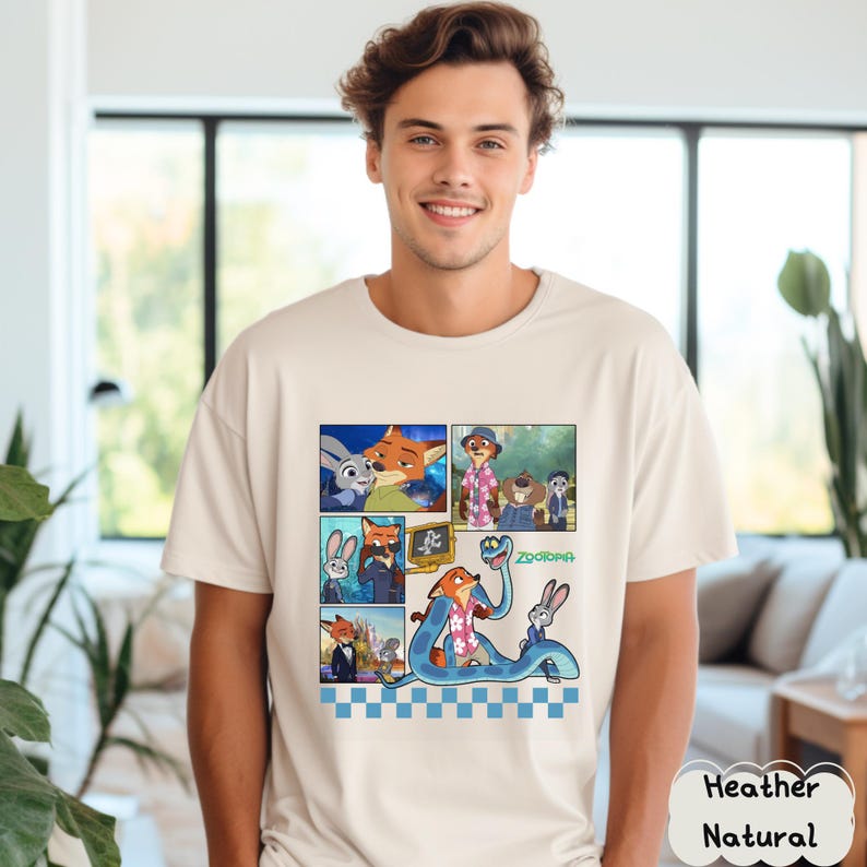 May include: A heather natural t-shirt featuring a colorful comic strip design with characters from the animated movie "Zootopia." The design includes images of a fox, a rabbit, and other characters. The word "Zootopia" is also visible.
