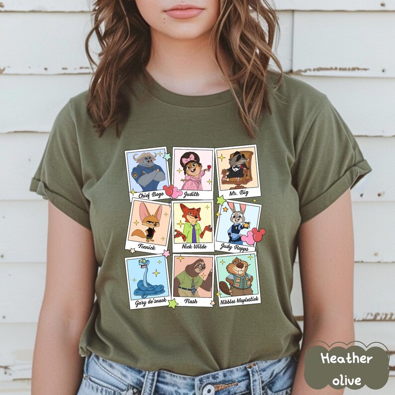 Peut inclure: T-shirt vert olive chin&eacute; avec une grille de portraits de personnages de dessins anim&eacute;s dans des cadres de style polaroid. Les personnages incluent Chief Bogo, Judith, Mr. Big, Finnick, Nick Wilde, Judy Hopps, Gary de'snack, Flash et Nibbles Maplestick.