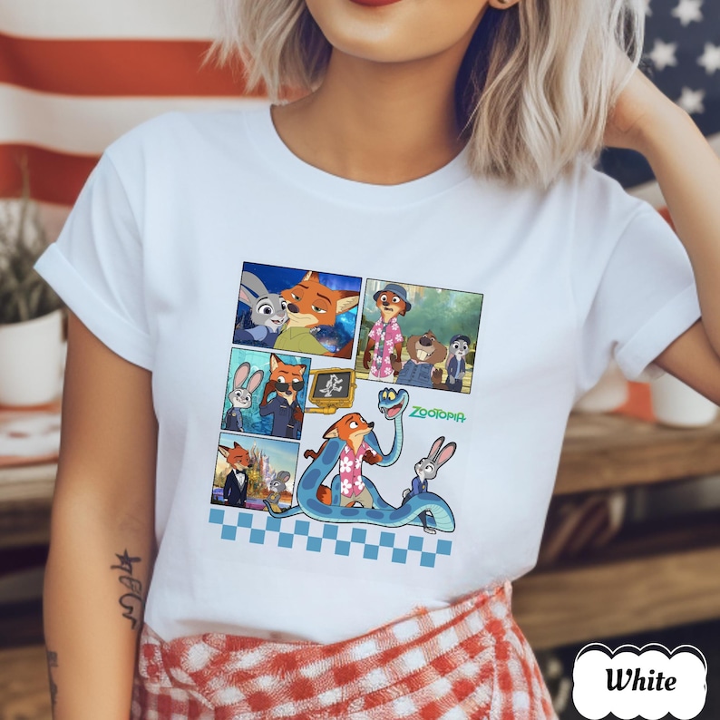 May include: White t-shirt featuring a colorful comic strip design with characters from the animated movie "Zootopia." The design includes images of a fox, a bunny, and other characters. The word "Zootopia" is written in green. The shirt has short sleeves.
