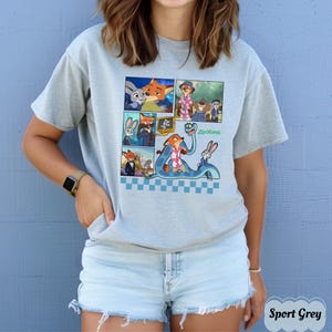 May include: Sport grey t-shirt featuring a comic strip design with characters from the animated movie Zootopia. The design includes images of a fox, a rabbit, and other characters. The word "Zootopia" is printed in green.