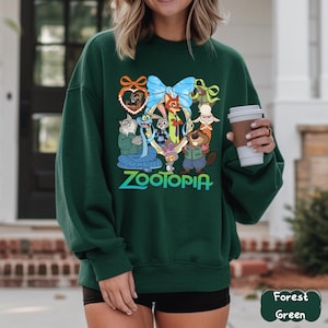 K&ouml;nnte beinhalten: Dunkelgr&uuml;nes Sweatshirt mit einem farbenfrohen Grafikdesign von Charakteren aus dem Animationsfilm Zootopia. Das Design zeigt eine blaue Schleife, das Wort "Zootopia" und verschiedene Tierfiguren. Das Sweatshirt ist einfarbig.