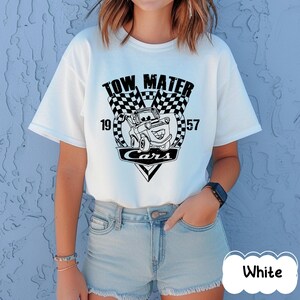 May include: White t-shirt with a black and white graphic of Tow Mater from the Cars film. The design includes the text "TOW MATER", "CARS", and the numbers "19" and "57". The shirt has short sleeves and a crew neck.