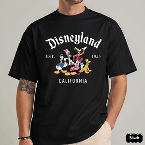 May include: Black t-shirt featuring a Disneyland graphic with Mickey Mouse, Minnie Mouse, Donald Duck, Daisy Duck, Goofy, and Pluto. The design includes the text "Disneyland" above "EST. 1955 CALIFORNIA".
