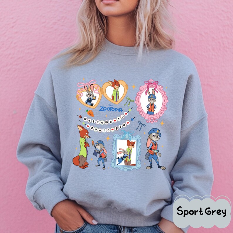 May include: Sport Grey sweatshirt featuring a colorful graphic of characters from the Disney movie Zootopia. The design includes framed portraits of the characters, the movie title, and the phrase "welcome to zootopia".