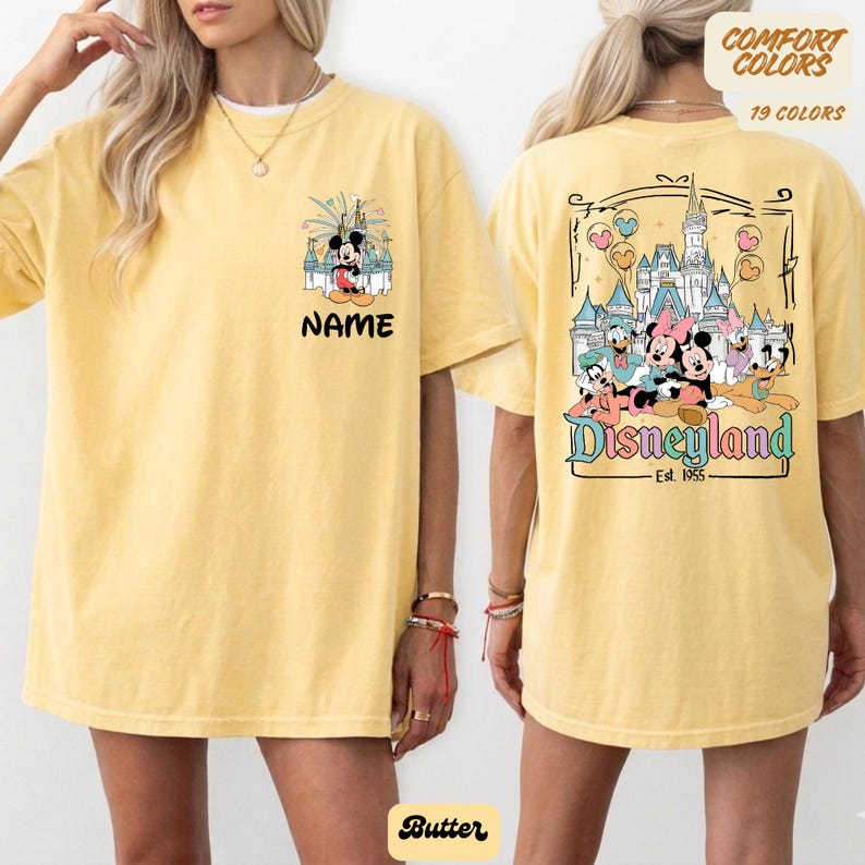 Puede incluir: Camiseta amarilla mantequilla con dise&ntilde;os de Mickey Mouse y Disneyland. La parte delantera muestra a Mickey frente a un castillo con la palabra "NAME". La parte trasera presenta personajes de Disney y el logo de Disneyland, con "Est. 1955".