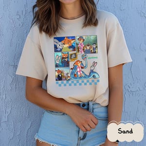 May include: Sand-colored t-shirt featuring a comic strip design with characters from the animated movie "Zootopia." The graphic includes images of a fox, a rabbit, and other characters. The word "Zootopia" is printed in green. The shirt has short sleeves.