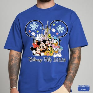 May include: Royal blue t-shirt featuring a graphic of Disney characters including Mickey and Minnie Mouse, Goofy, Donald and Daisy Duck. The design includes a castle and the text "Disney Trip 2020".