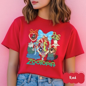 Może przedstawiać: Czerwona koszulka z kolorową grafiką postaci z filmu "Zwierzogr&oacute;d". Projekt zawiera niebieską kokardę, złotą ramkę i słowo "Zootopia" w kolorze zielonym. Koszulka jest wykonana z miękkiego materiału.