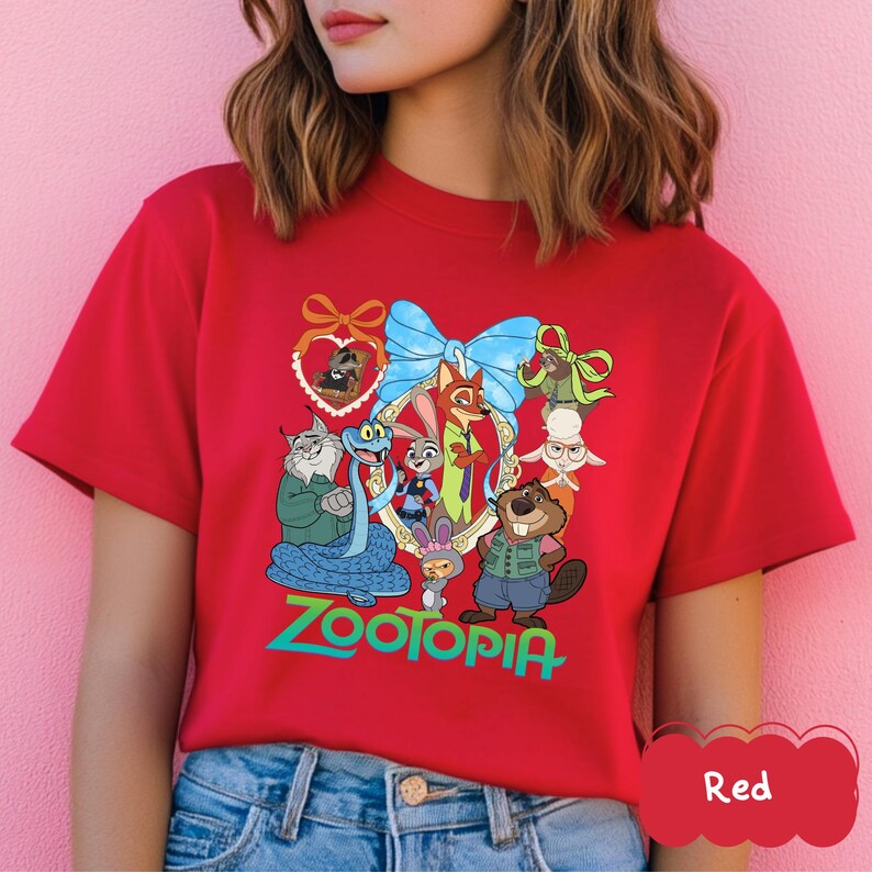 Może przedstawiać: Czerwona koszulka z kolorową grafiką postaci z filmu "Zwierzogr&oacute;d". Projekt zawiera niebieską kokardę, złotą ramkę i słowo "Zootopia" w kolorze zielonym. Koszulka jest wykonana z miękkiego materiału.
