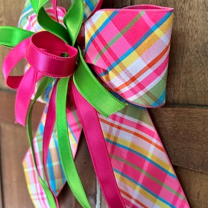 Peut inclure: Un nœud décoratif avec des rubans roses vifs, verts et à carreaux. Le nœud a un grand design multicouche avec de longs rubans fluides. Le motif à carreaux comprend du rose, du jaune, du bleu et du vert. Le nœud est probablement utilisé pour la décoration.