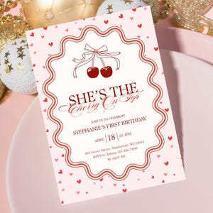 Op de afbeelding: Een roze uitnodigingskaart met een geschulpte rand en rode hartaccenten. De kaart bevat de tekst "SHE'S THE Cherry On Top" en details voor een eerste verjaardagsviering, inclusief datum, tijd en locatie.
