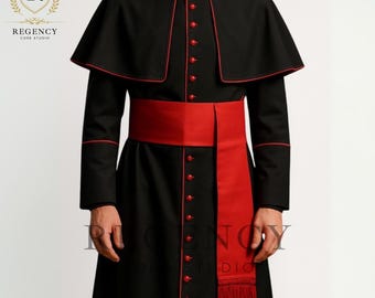 May include: A black clerical cassock with red trim and buttons. The garment features a red sash and a matching cape. The outfit is formal and traditional, suitable for religious ceremonies. The Regency Core Studio logo is visible in the upper left corner.
