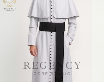Pode incluir: Uma túnica clerical branca com uma faixa e franjas pretas. A túnica tem uma gola alta e é abotoada na frente. As mangas são compridas e a peça é usada com um cinto preto. O texto "REGENCY CORE STUDIO" é visível.