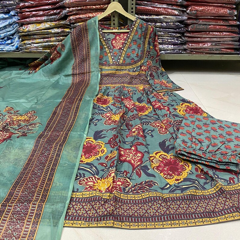 May include: A teal-colored, floral-patterned dress with matching pants and a scarf. The dress features a V-neck and long sleeves. The floral pattern includes red, yellow, and purple flowers. The scarf has a patterned border.
