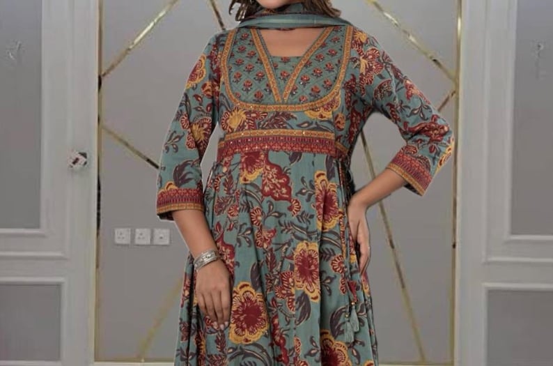 May include: A teal-colored dress with a floral pattern in red and yellow. The dress has long sleeves and a V-neckline with a matching scarf. The waist is cinched with a red and gold band. The dress is a flowing, feminine style.