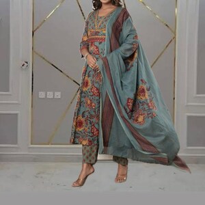May include: A three-piece teal floral print outfit. The set includes a long-sleeved tunic, matching pants, and a flowing scarf. The tunic and scarf feature a red and yellow floral pattern. The outfit is made of a lightweight fabric.