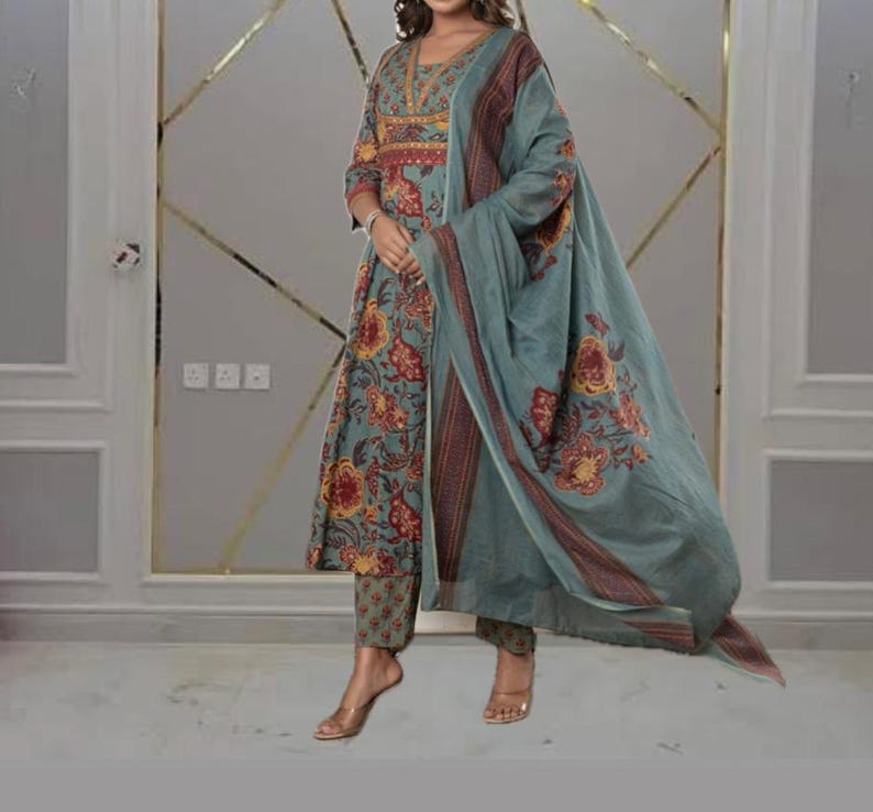 May include: A three-piece teal floral print outfit. The set includes a long-sleeved tunic, matching pants, and a flowing scarf. The tunic and scarf feature a red and yellow floral pattern. The outfit is made of a lightweight fabric.