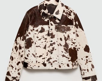 May include: A cowhide jacket with a classic collar and button-down front. The jacket features a brown and white spotted pattern, with two chest pockets and two side pockets. The jacket is a medium weight and suitable for cooler weather.