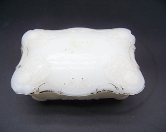May include: White porcelain trinket box with a raised floral design. The box has a slightly scalloped edge and sits on four small feet.