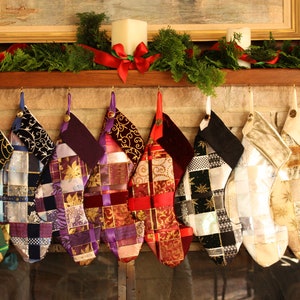 May include: Nine colorful patchwork stockings hang on a fireplace mantel. The stockings are made of various fabrics and ribbons, and each has a unique design. The stockings are decorated with gold, silver, red, purple, and green accents.