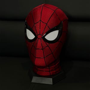 以下が含まれることがあります： 白メッシュのアイカバーが付いた赤と黒のスパイダーマンマスク。マスクはクモの巣模様で、黒いスタンドに展示されています。マスクは、スーパーヒーローの象徴的なヘッドウェアのレプリカです。