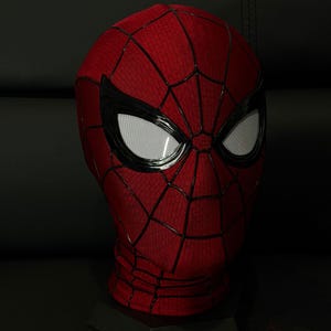 以下が含まれることがあります： 赤と黒のスパイダーマンマスク、クモの巣模様。 マスクには、黒で縁取られた白いメッシュの目があります。 マスクは、暗い背景に対して黒いスタンドに表示されています。