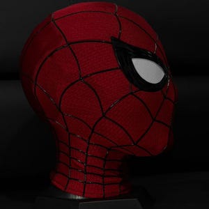 以下が含まれることがあります： クモの巣模様の赤と黒のスパイダーマンマスク。マスクは白いメッシュの黒い目の覆いがあり、黒いスタンドに展示されています。マスクはテクスチャード加工された生地で作られています。