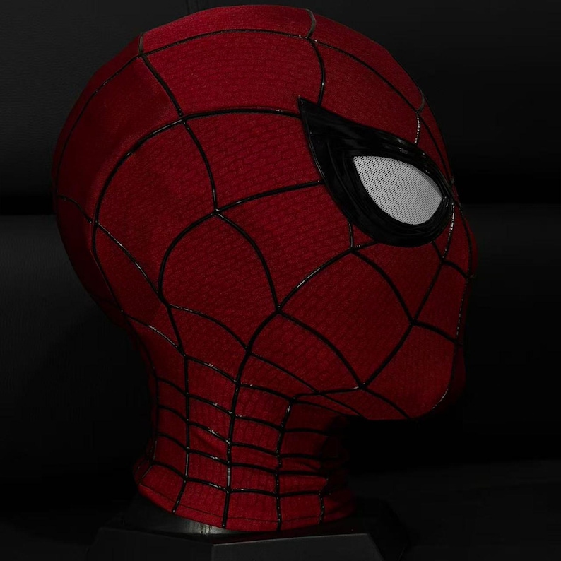 以下が含まれることがあります： クモの巣模様の赤と黒のスパイダーマンマスク。マスクは白いメッシュの黒い目の覆いがあり、黒いスタンドに展示されています。マスクはテクスチャード加工された生地で作られています。
