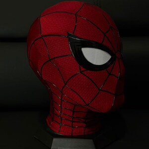 以下が含まれることがあります： 赤と黒のスパイダーマンマスク、クモの巣模様。 マスクは白いメッシュの目の覆いがあり、黒いスタンドに展示されています。 マスクは頭全体を覆っています。